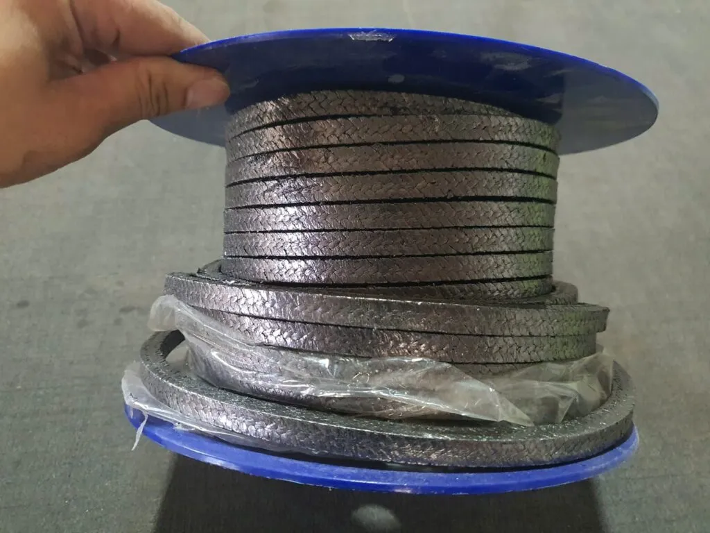 Dây tết chèn graphite cuộn cầm trên tay, các vòng dây dưới đáy bọc nilon