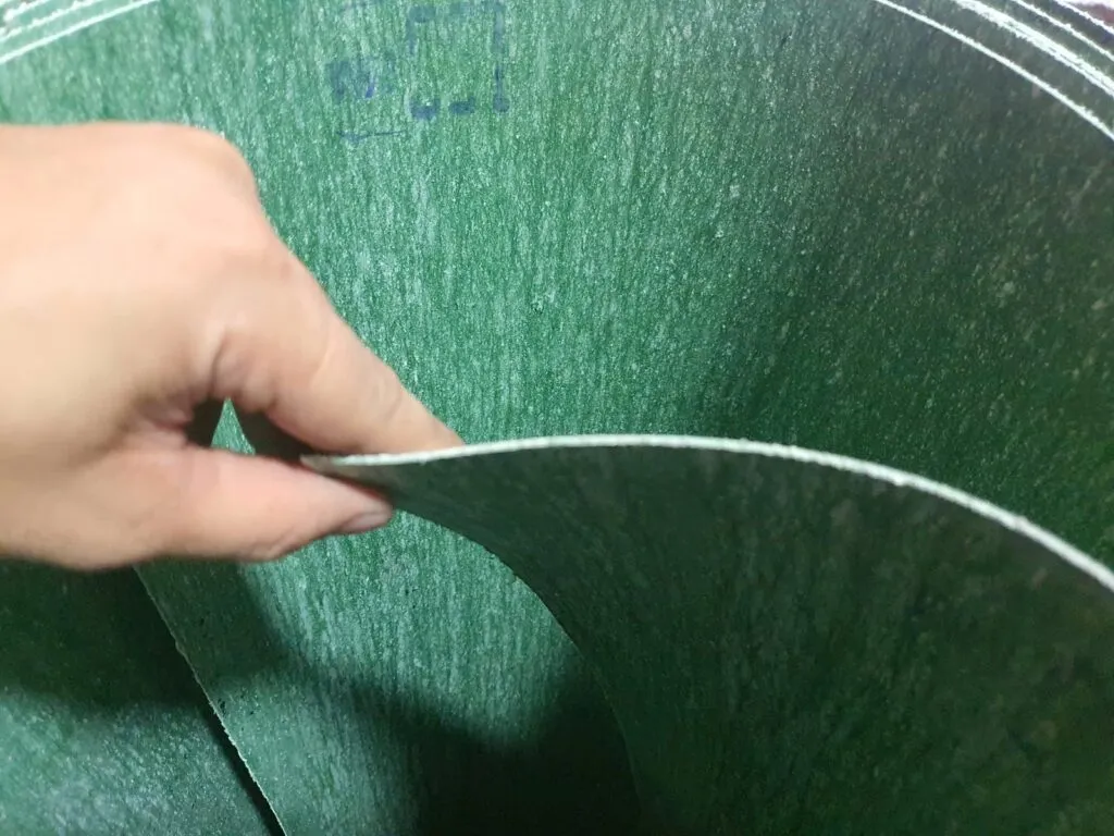 Tấm amiang chịu dầu màu xanh lá, tay lật mép tấm cho thấy mặt bìa vân sợi